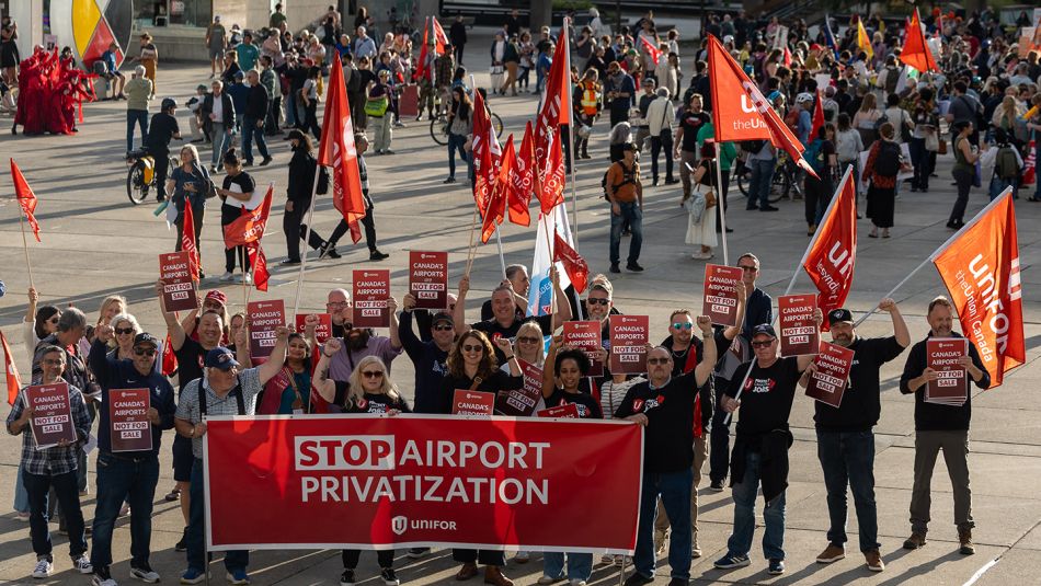 A group of people holding a red Unifor banner and flags