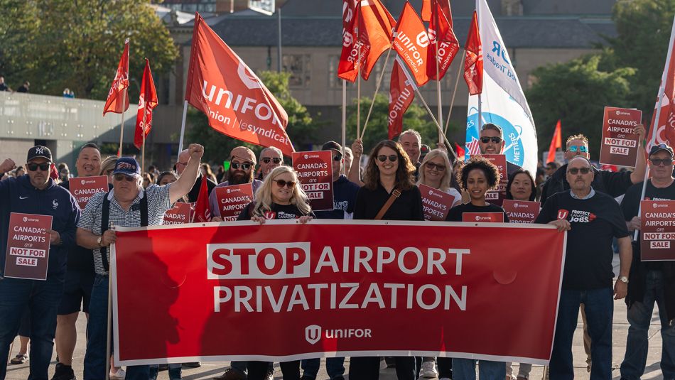 A group of people holding a red Unifor banner and flags
