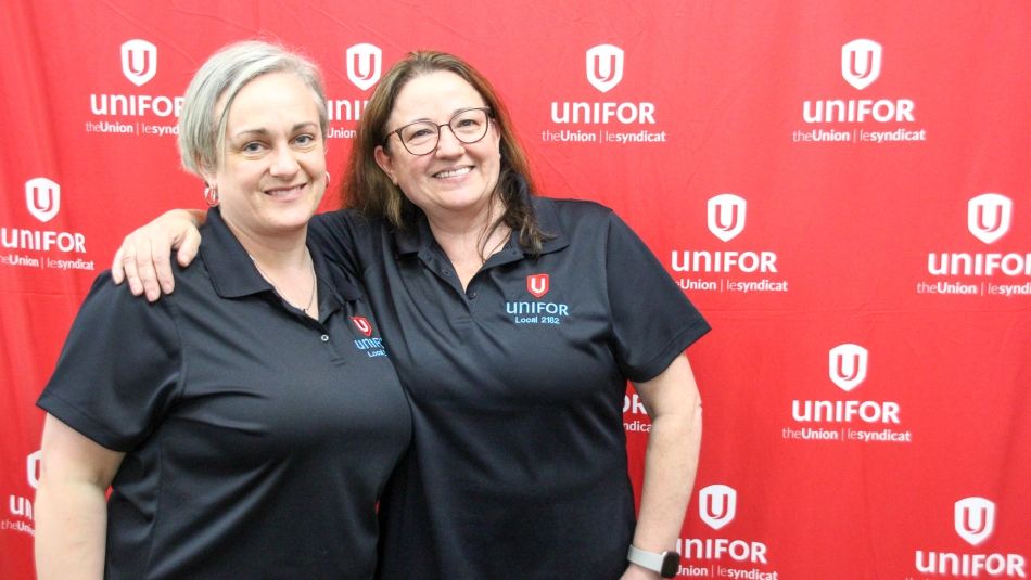 Two women in front a Unifor banner smiling
