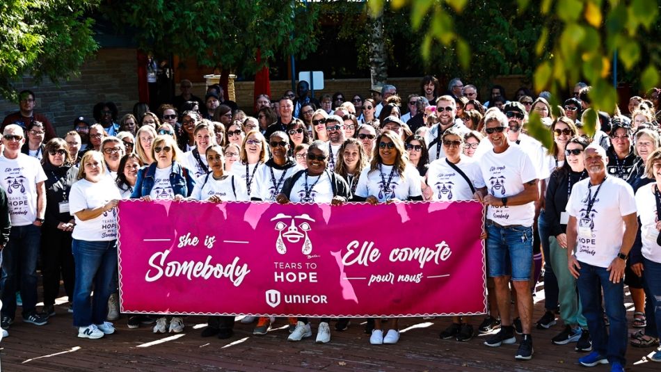 Large group posing with a pink banner reading She is Somebody.