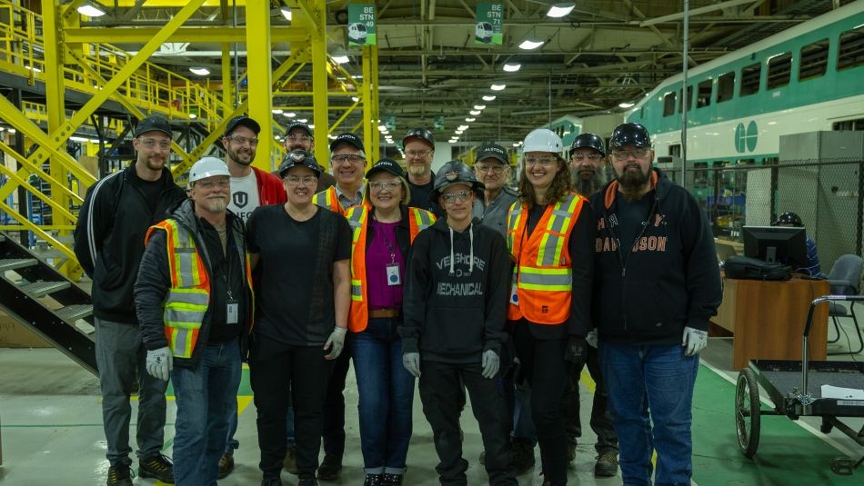 A group of people in safety gear with a GO Train in the background.