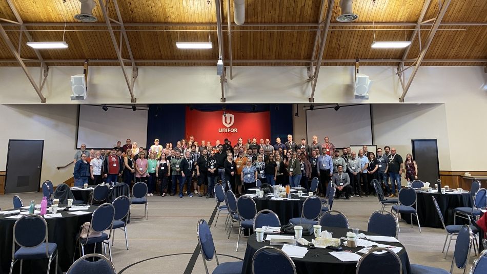 A group of people standing in front of a red Unifor stage with chairs and tables in the foreground.