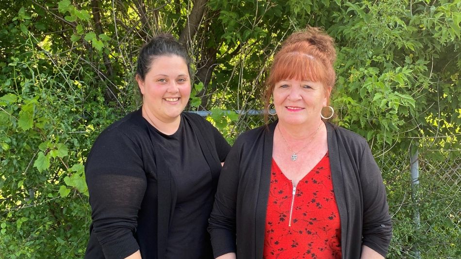 Two women posing outside in front of green foliage