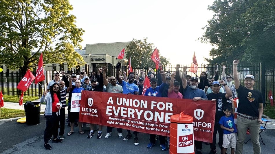 Un groupe de personnes debout derrière une bannière rouge d'Unifor