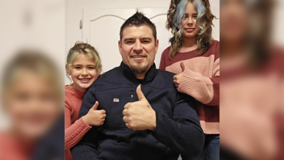 Tyrone McLeod posing with two young girls. All are giving a 'thumbs up' sign.