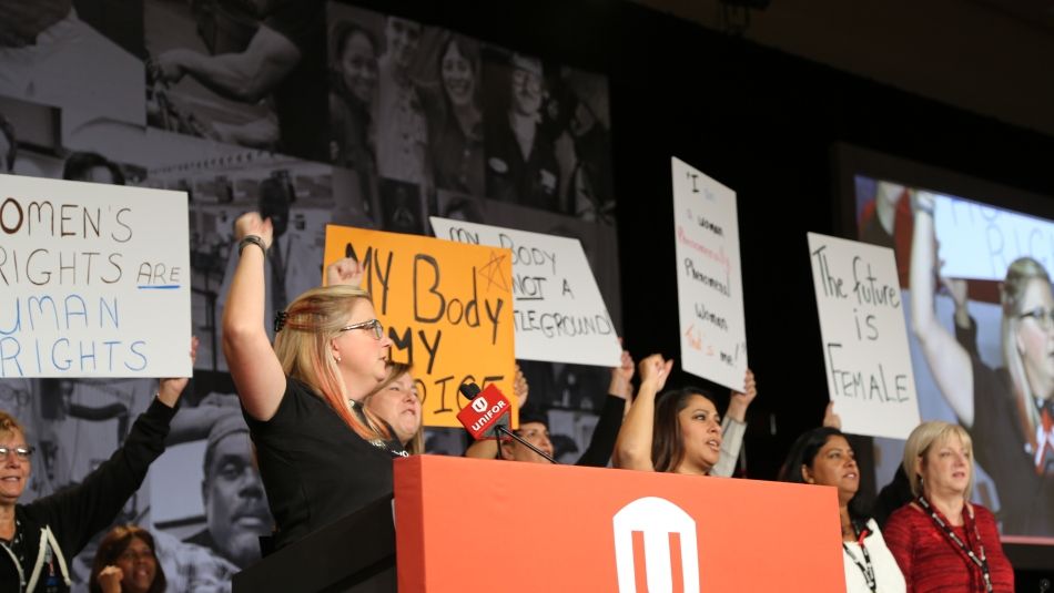 Unifor women on stage at council holding up women's rights signs