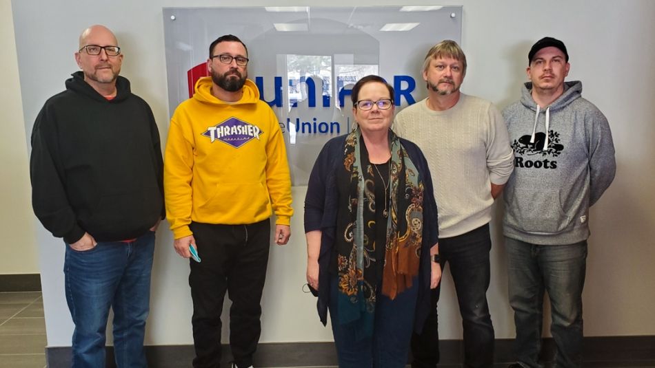 Five Local 1256 members posing for a photo indoors in front of a Unifor sign.