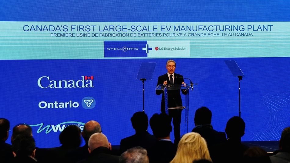 Stellantis-LG announcement Man in suit on stage in front of a large screen with Canada's First Large Scale EV Manufacturing Plant