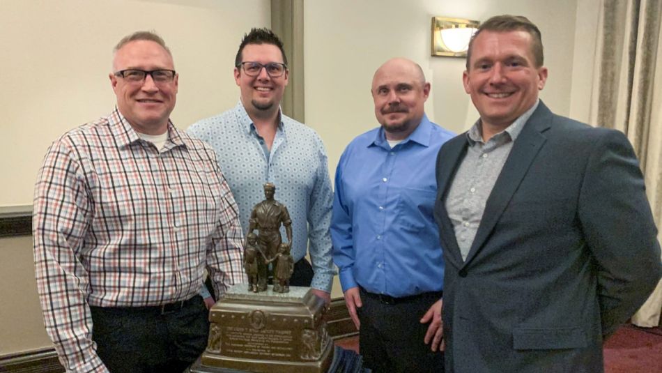 Four people posing for photo with a trophy.