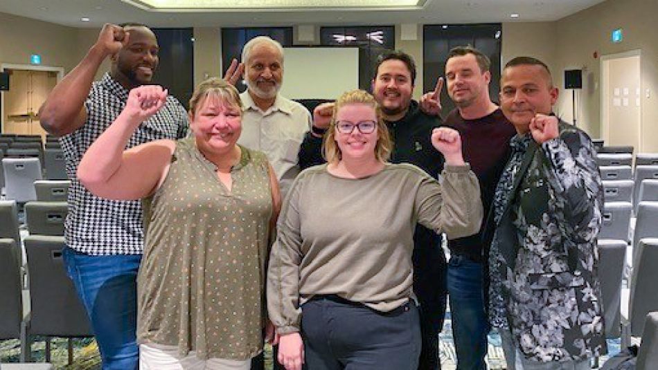 Seven people standing in a meeting room posing for photo with fists in the air