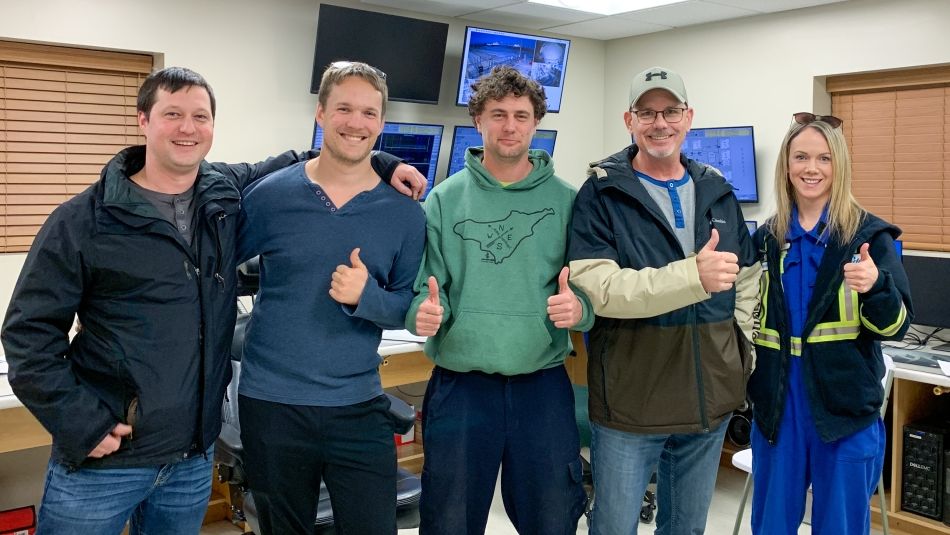 Five smiling people posing in a control room giving the thumbs up.