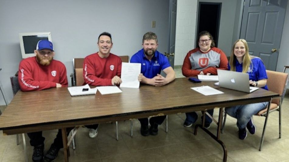 Five people seated at a folding table. One holds up a document.