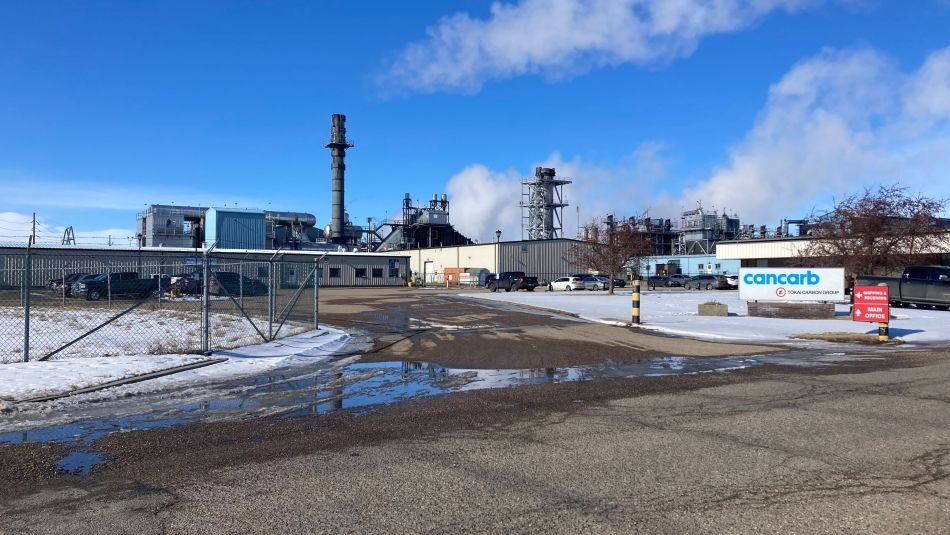 Industrial facility with a smoke stack with Cancarb signage near the front gate. 