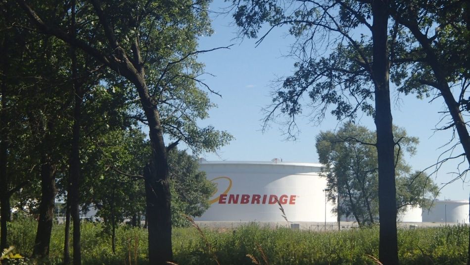 Grand réservoir de carburant liquide avec le logo d'Enbridge. Arbres au premier plan. 