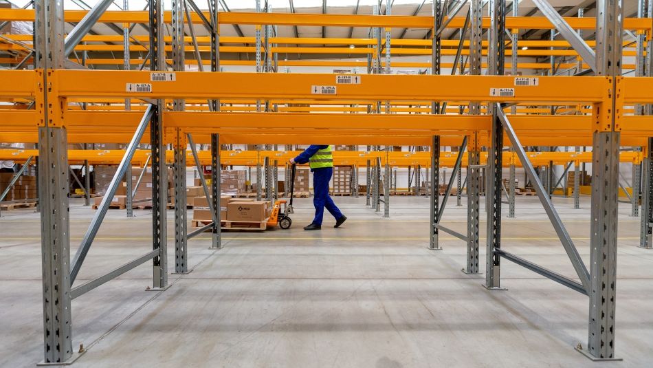 A worker pushes a hand-truck in a large warehouse.