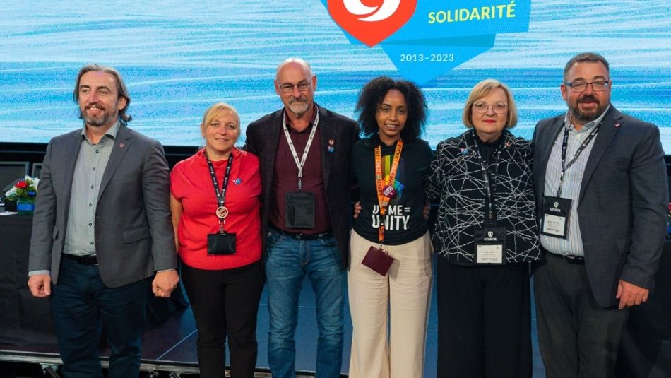 Three men and three women posing for a photo together in front of a video screen with a Unifor 10th anniversary logo.