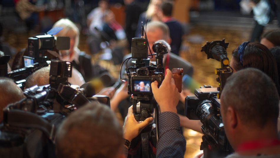 reporters holding up cameras pointed at a person 
