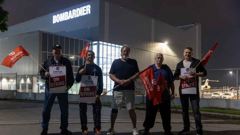Unifor Local 112 and 673 members standing on the picket line in front of the Bombardier facility at Pearson Airport holding on strike signs and red Unifor flags