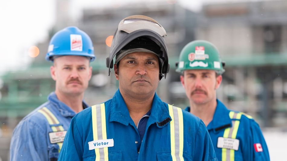 Three workers in hard hats and matching blue coveralls.