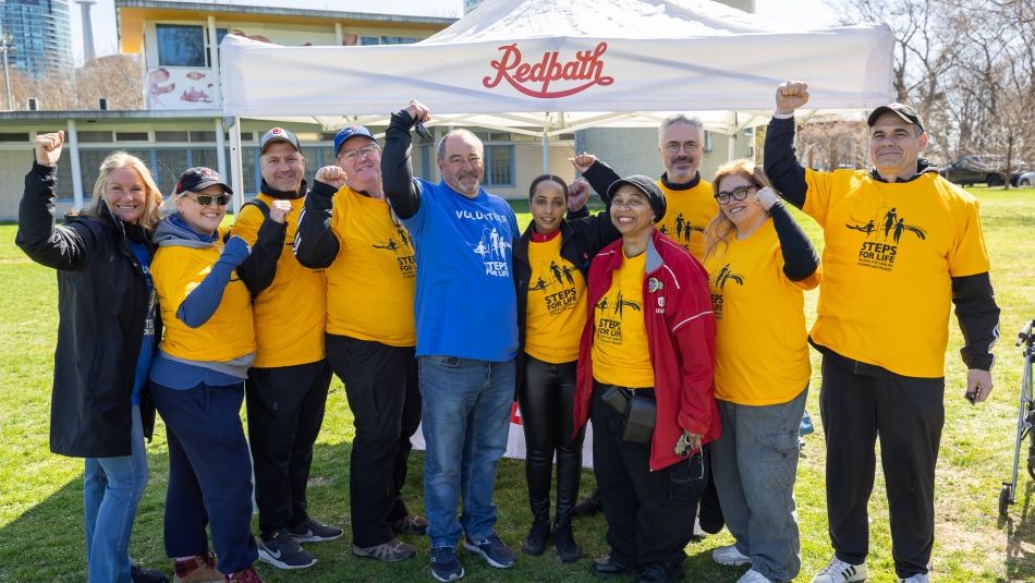 A group of people fists raised wearing yellow "Steps for Life" t-shirts" standing in front of a Redpath tent