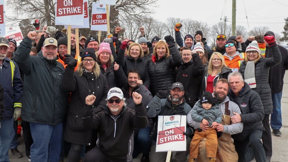 Windsor Salt picket line Lana Payne among a large group of workers outdoors holding On Strike placards and holding fists in the air