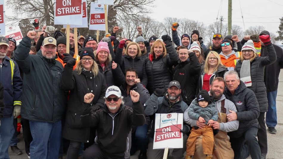 Lana Payne among a large group of workers outdoors holding On Strike placards and holding fists in the air