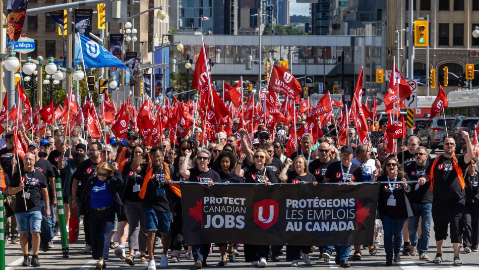 A crowd in front of Parliment Hill in Ottawa behind a Protect Canadian Job banner and a sea of red Unifor flags