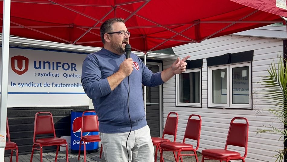 Man speaking into a microphone with Unifor banner in the background