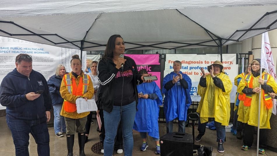 A women speaking under a tent to a group wearing rain coats.