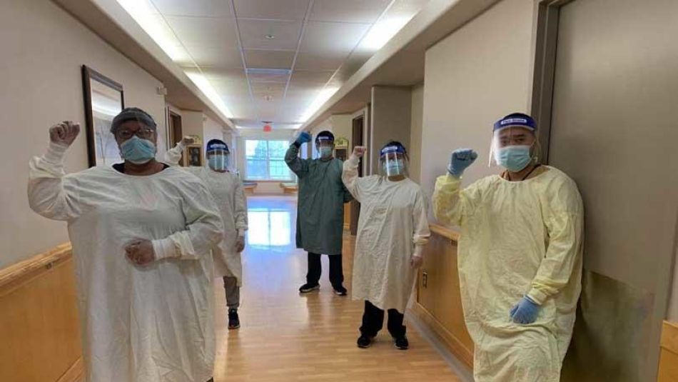 Five health care workers on the job in full PPE raise their fists in solidarity.
