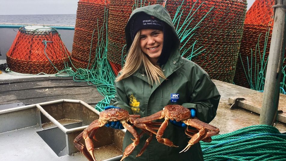 A fisherwoman holding up two crabs on a boat at sea.