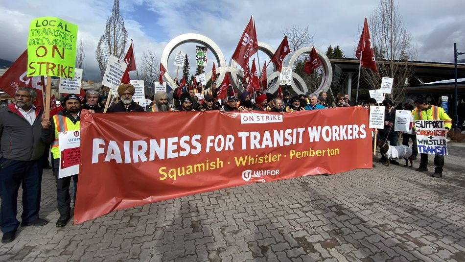 Transit workers' rally in Whistler Grande foule devant les anneaux olympiques de Whistler tenant des drapeaux et une grande bannière « Équité pour les travailleurs du transport en commun »