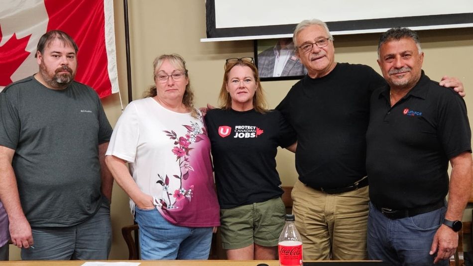 A group of five people standing at a table with papers on them.