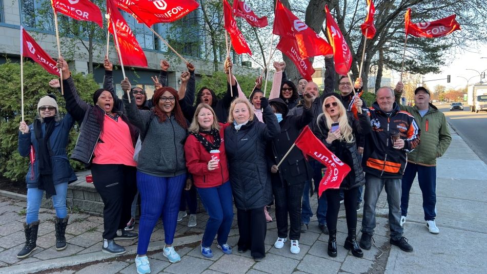 A group of people waving red Unifor flags outside of a building.