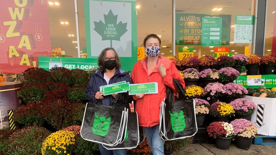 Two women outside Food Basics grocery store holding information postcards. 