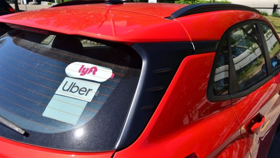 Lunette arrière d’une voiture rouge avec autocollants Lyft et Uber visibles.