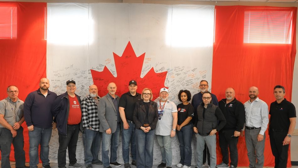 Unifor cami leadership in front of a large Canadian flag full of signatures