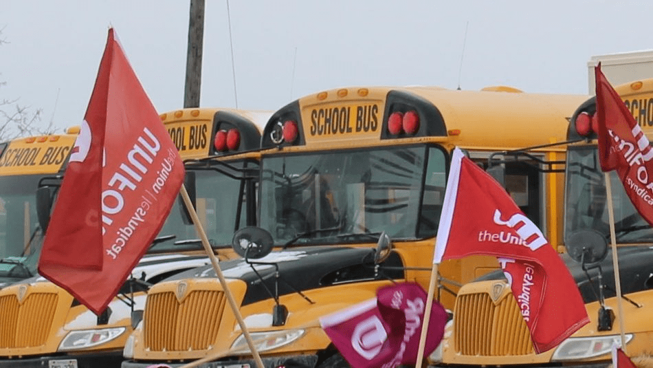 Des bus scolaires jaunes avec des drapeaux rouges d'Unifor au premier plan.