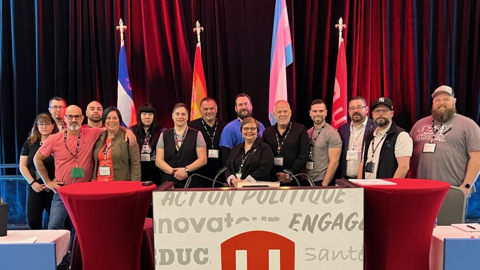 A group of people smile while standing in front of a large white Unifor sign with the red shield logo.