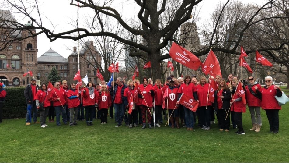 Unifor delegation in front of the legistlative building wearing red Unifor shirts waving our flags