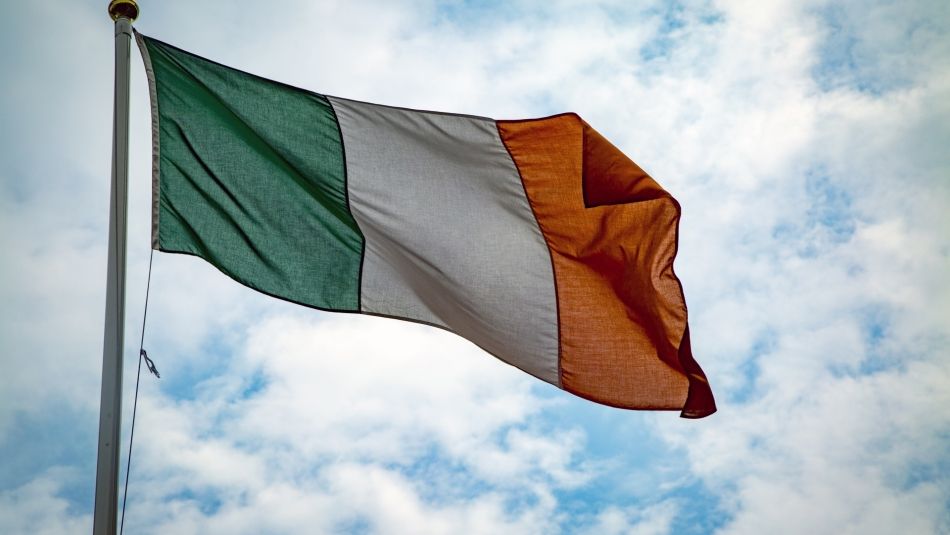 “View from below of an Irish flag at the top of a flagpole against the sky.”