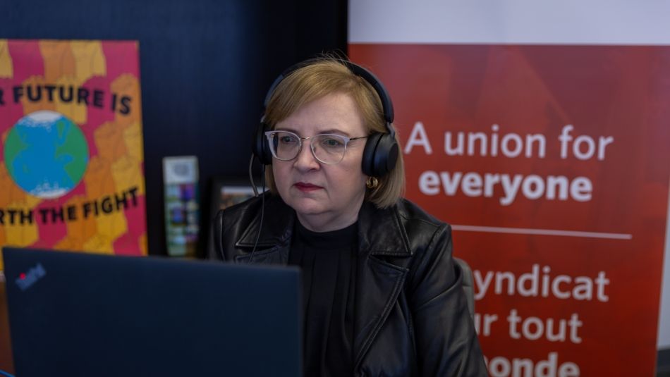 A woman wearing a headset sits at a computer screen.