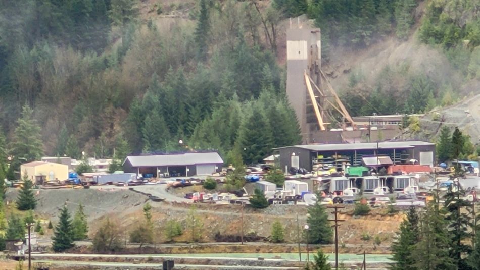 Wide shot of a mine site, including some buildings, a tailing pond in the foreground and forest in the background.