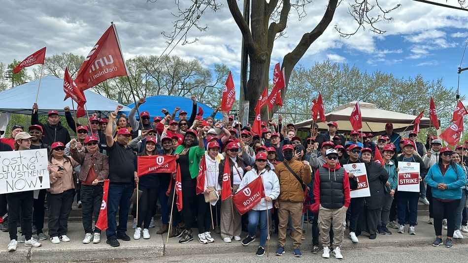 Une grande photo de groupe de personnes tenant des drapeaux d'Unifor, des cartons de table et des pancartes de grève.