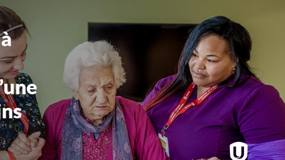Une préposée aux services de soutien à la personne de race noire aide une personne âgée à se lever dans une maison de soins de longue durée