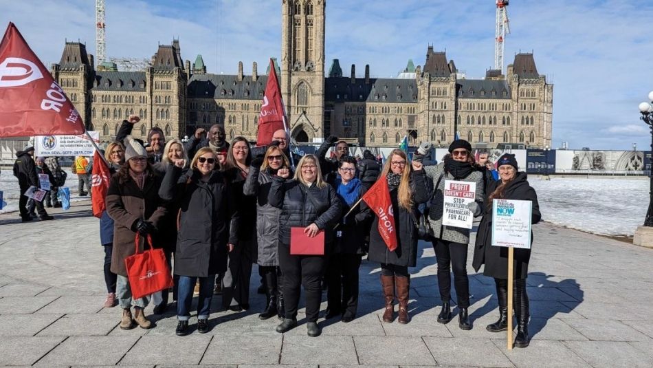 A large group standing outside the legislature building holding placcards