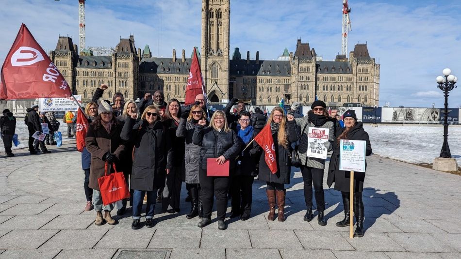 Un groupe de personnes se tient devant la Colline du Parlement avec des pancartes réclamant un régime d'assurance-médicaments.