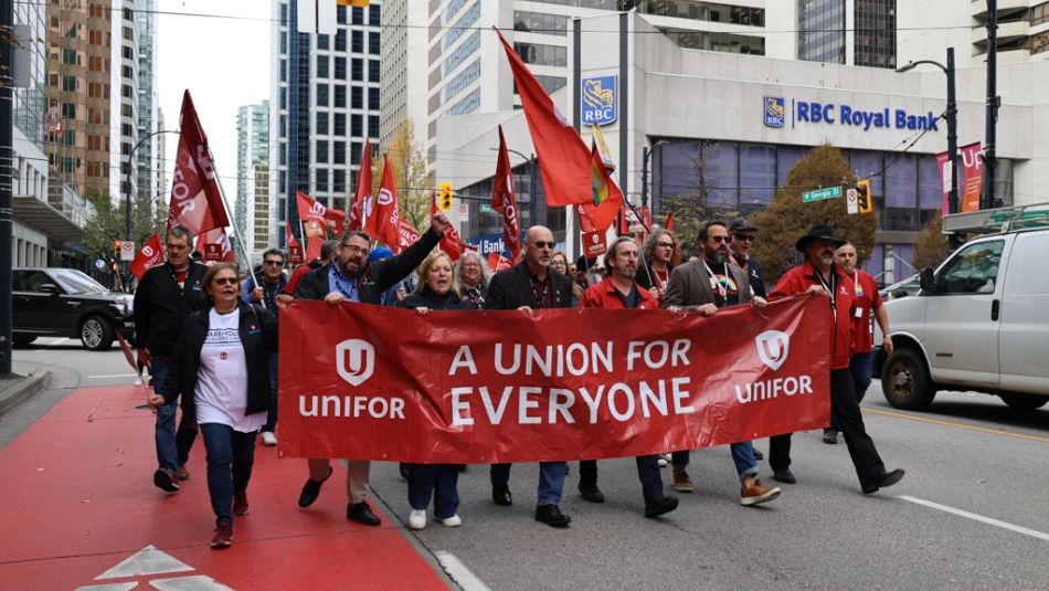 Rally in Vancouver People marching down a city street with flags and a banner reading Unifor A union for everyone.