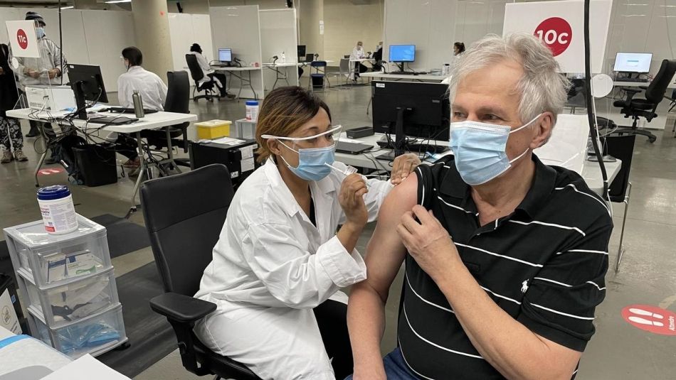 Renaud Gagné wears a mask while receiving a vaccination from a health care worker in a mask and faceshield.