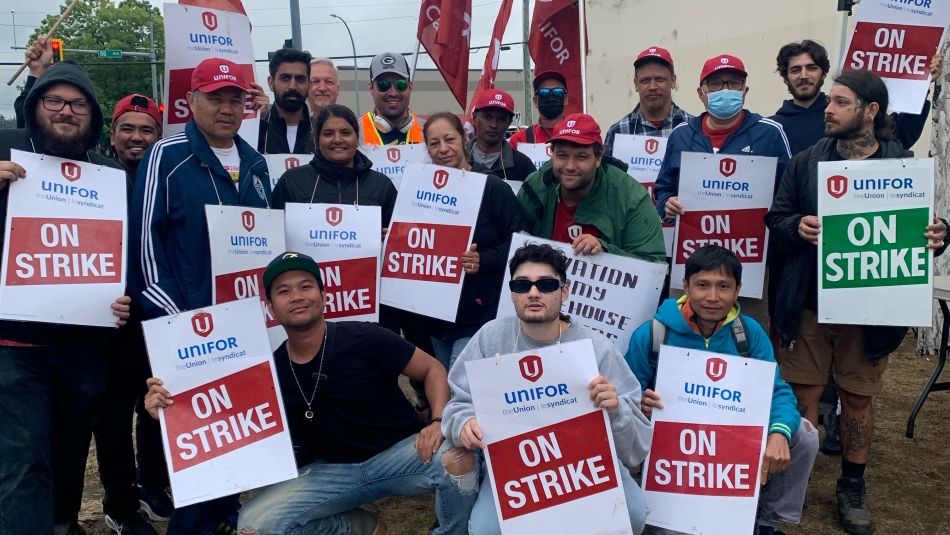 A dozen or so workers holding On Strike placards outside of a Salvation Army warehouse